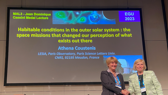 Two women shaking hands on a podium in front of a screen projecting text from the European Geosciences Union